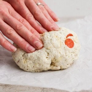 Hands forming a ball of pizza protein bagel dough with herbs and pepperoni