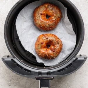 Two baked pizza protein bagels with Italian seasoning in an air fryer basket