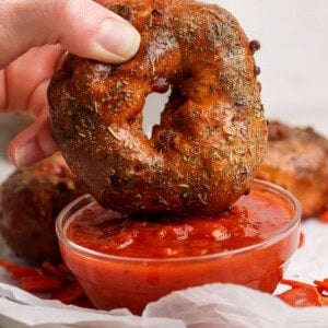Hand dipping a pizza protein bagel into a bowl of marinara sauce