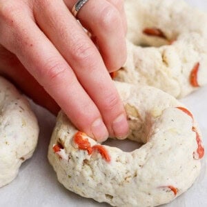 Hand shaping pizza protein bagel dough with pepperoni pieces on parchment paper