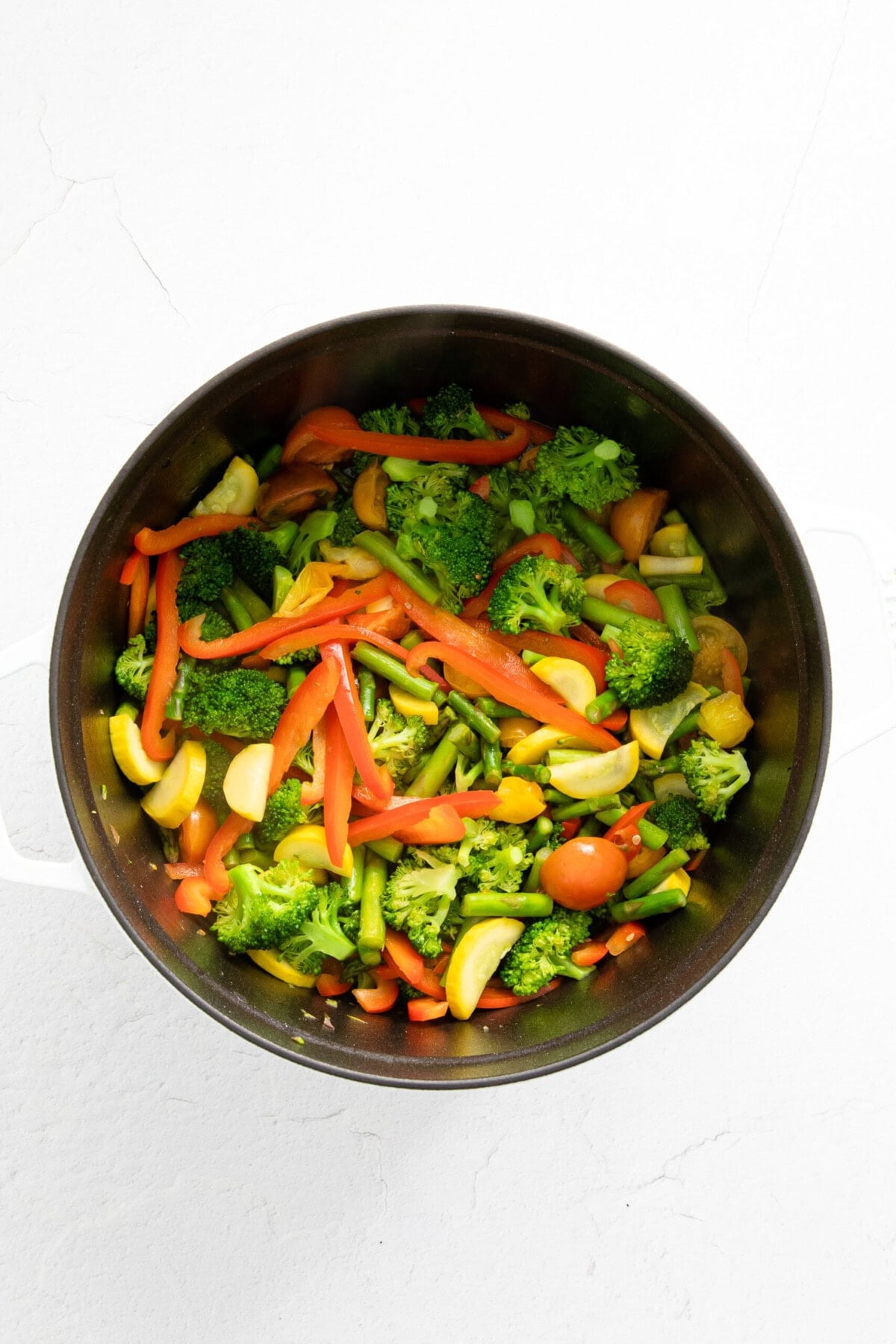 A white surface with a pan of pasta primavera containing vegetables.