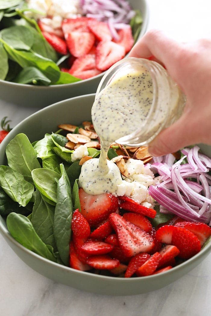 Pouring poppy seed dressing over a strawberry spinach salad.
