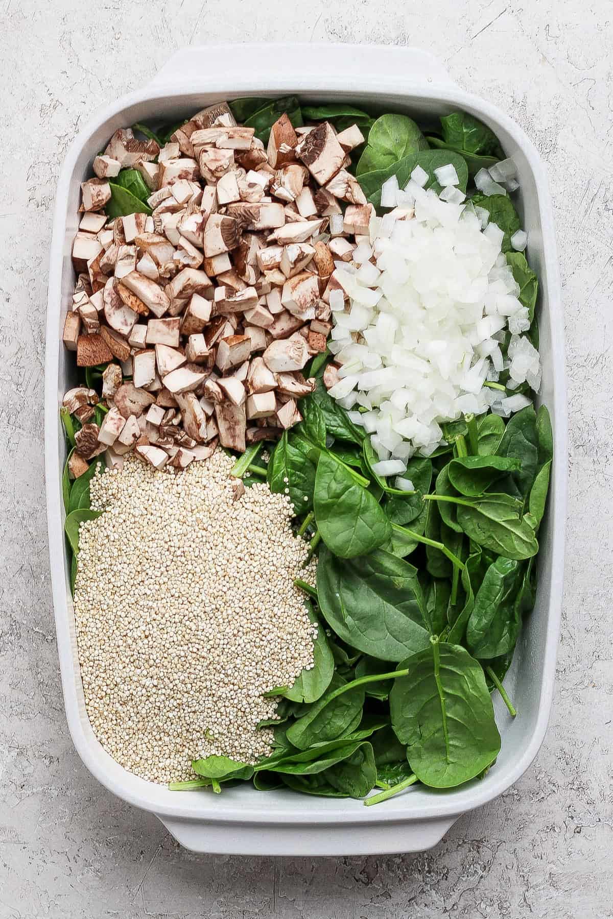 Chopped mushrooms, diced onion, fresh spinach, and uncooked quinoa in a baking dish