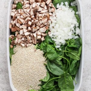 Chopped mushrooms, diced onion, fresh spinach, and uncooked quinoa in a baking dish