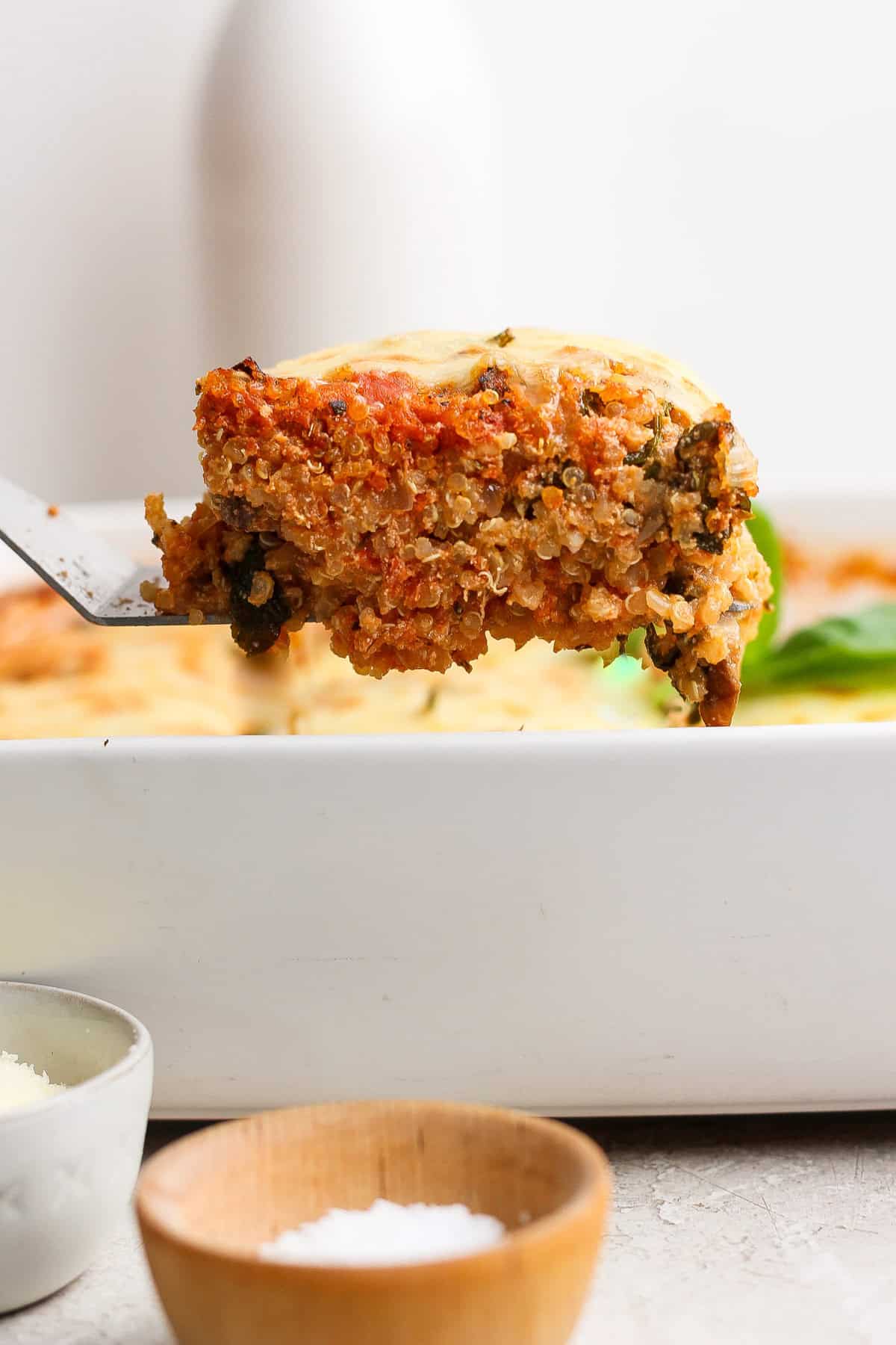 Lifting a slice of spinach quinoa lasagna casserole from the baking dish with a spatula