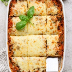 Full dish of spinach quinoa lasagna casserole cut into portions with fresh basil