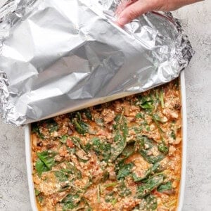 Covering spinach quinoa lasagna casserole with aluminum foil before baking