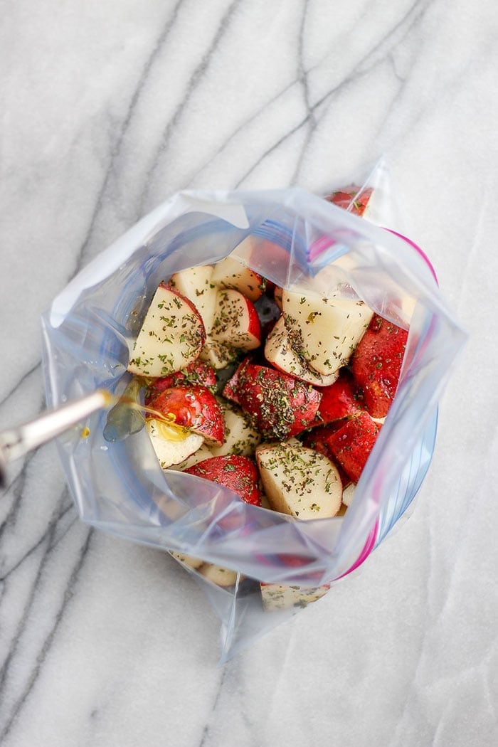 These grilled potatoes in foil are crispy, fork-tender, and ready in 30 minutes. Toss in olive oil and spices, wrap in foil, and grill for the easiest summer side! red potatoes and spices in a plastic bag