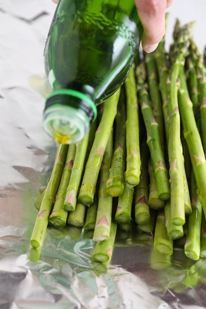drizzling olive oil over asparagus spears on a sheet of foil