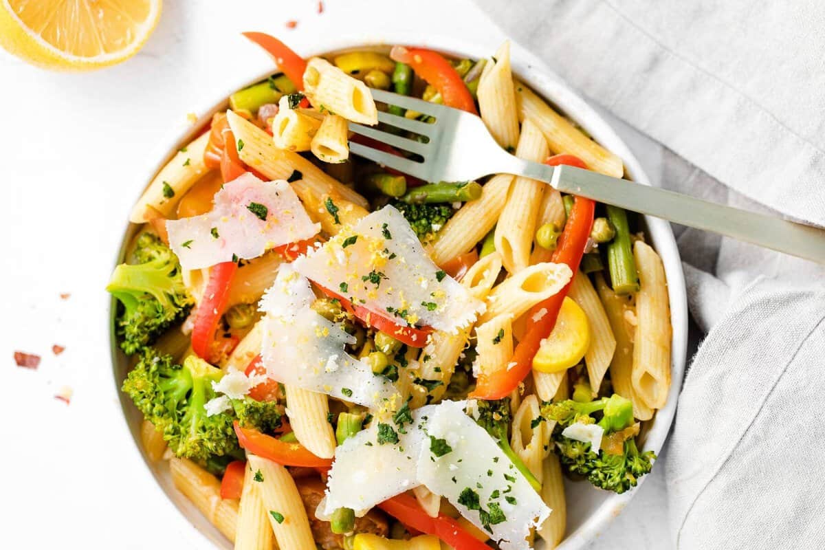 pasta primavera in a bowl topped with parmesan cheese and fresh basil
