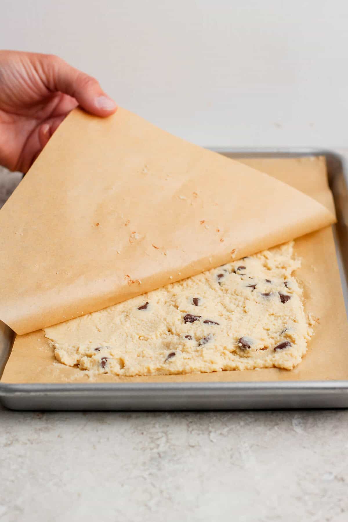 pressing cottage cheese cookie dough flat with parchment paper on a baking sheet