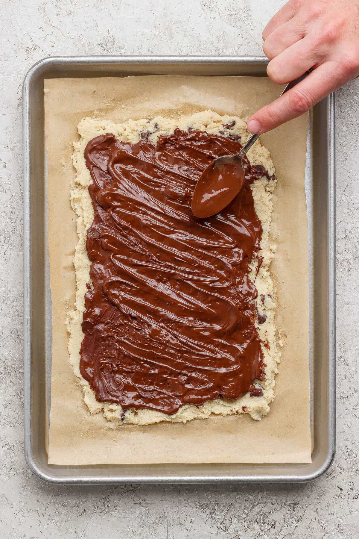 spreading melted chocolate over cottage cheese cookie dough bark with a spoon