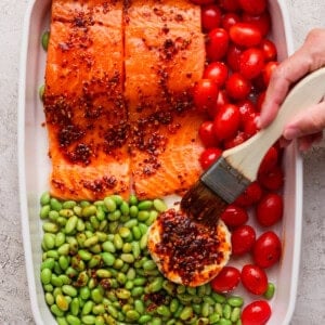 Brushing chili crunch onto Boursin cheese in a casserole dish with raw salmon and vegetables before baking