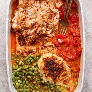 Baked salmon casserole with roasted tomatoes, edamame, and melted Boursin cheese with two gold forks in a white dish