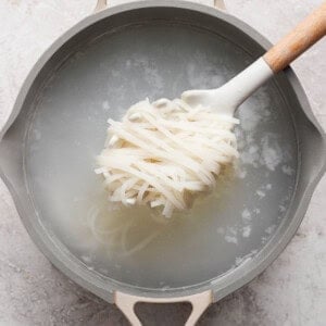 Rice noodles being lifted from a pot of boiling water with a spatula
