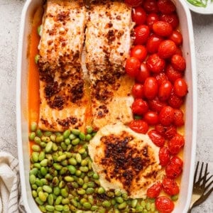 Close-up of baked chili crunch salmon with burst cherry tomatoes and edamame in a casserole dish