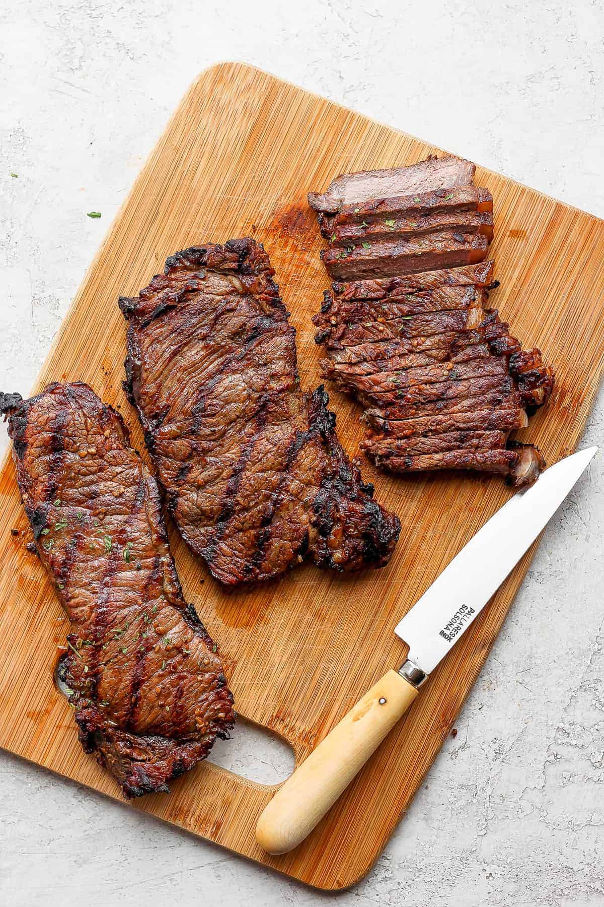 Seriously delicious steak salad made with perfectly grilled steak, avocado, tons of veggies, and an herby vinaigrette dressing. sliced cooked steak on cutting board.