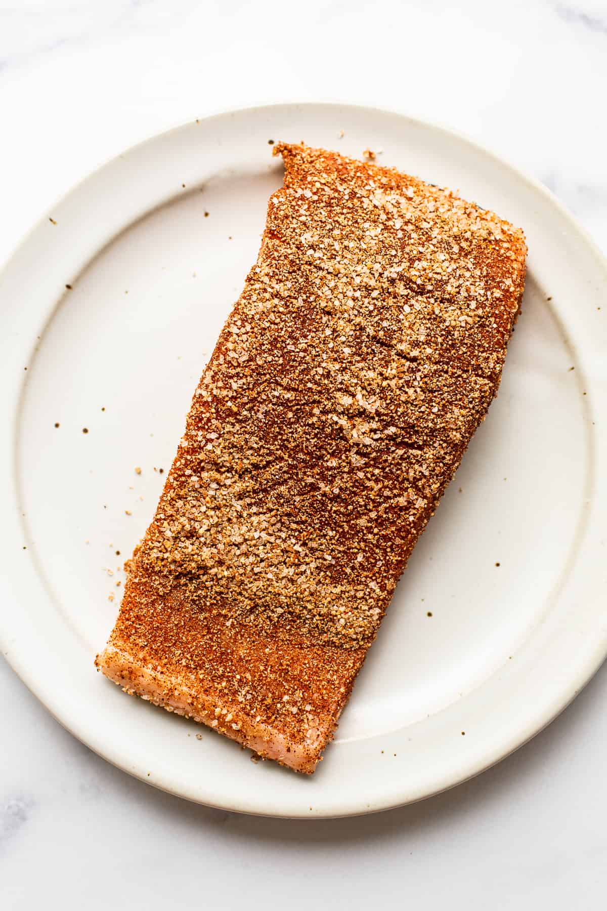 This perfectly tender and flakey smoked salmon is made with a simple dry rub and a yummy maple glaze making it perfect for crackers, bagels, or a salad! seasoned salmon on plate.