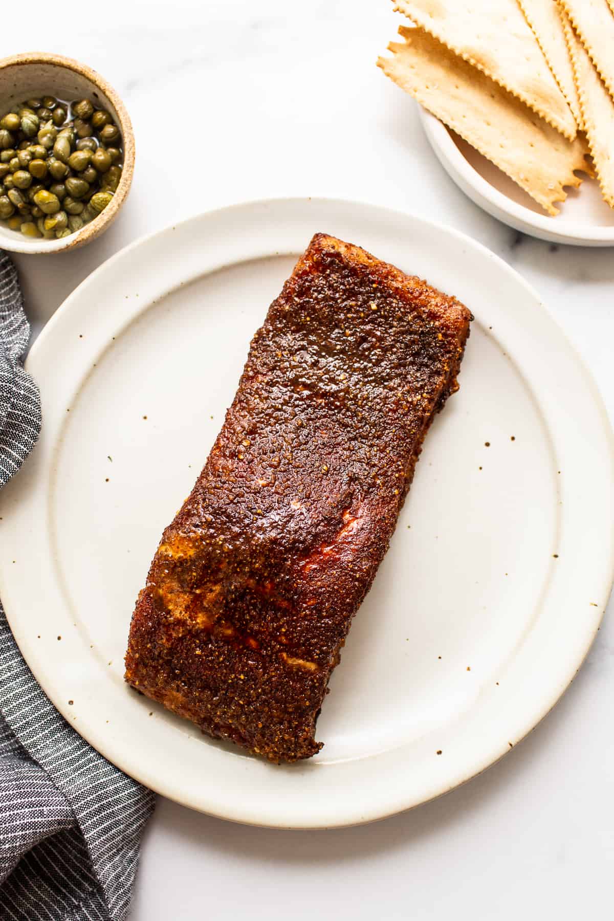 This perfectly tender and flakey smoked salmon is made with a simple dry rub and a yummy maple glaze making it perfect for crackers, bagels, or a salad! smoked salmon filet on plate.