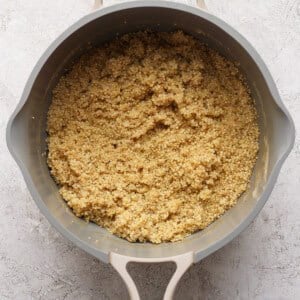 A top-down view of cooked quinoa in a light gray cooking pot on a textured light surface.