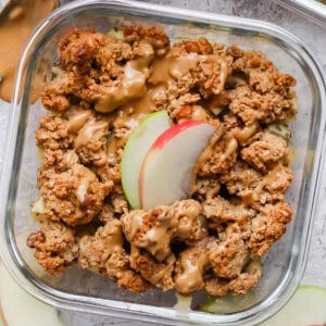 Protein apple crisp in a glass meal prep container topped with nut butter.