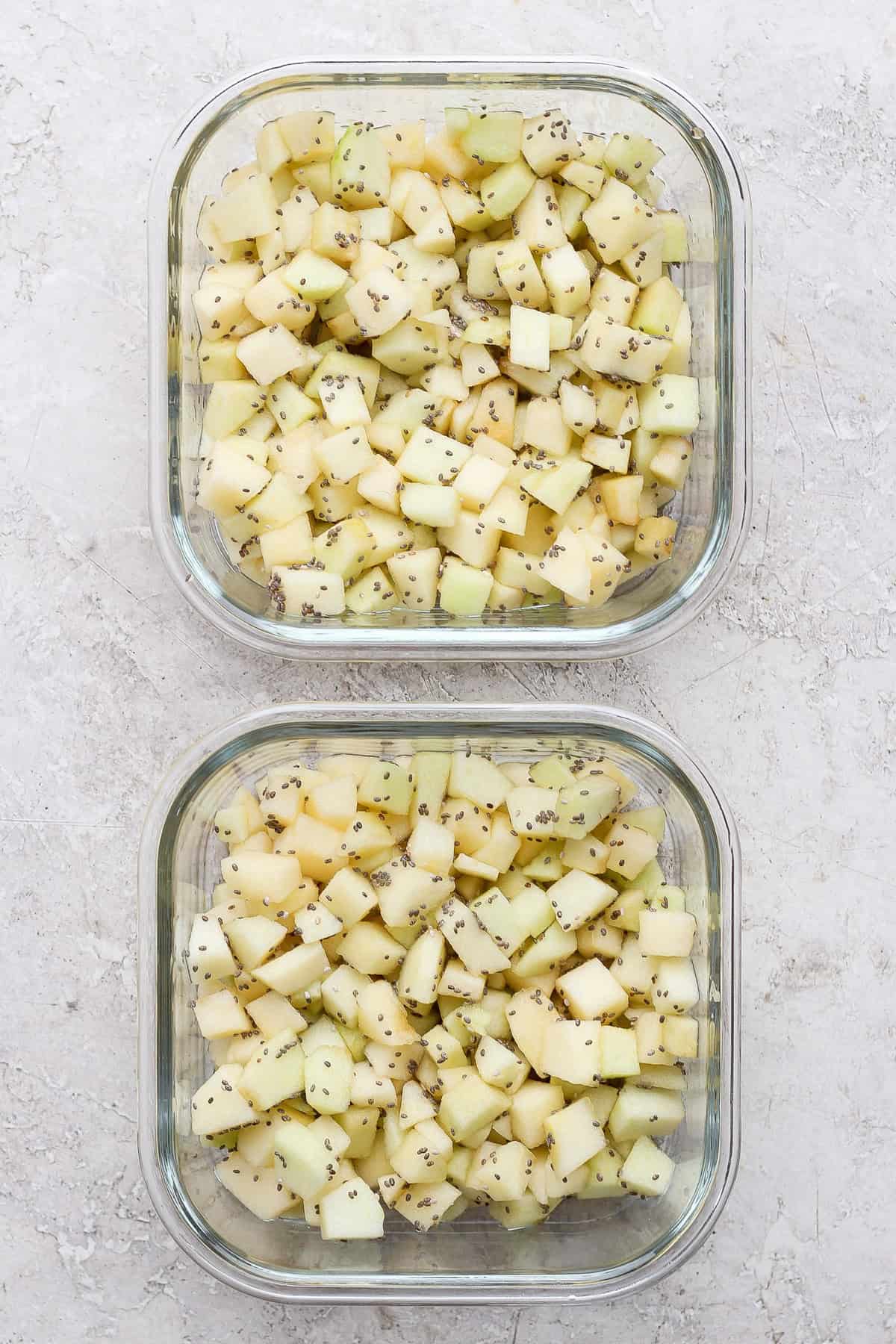 Diced apples divided between two glass meal prep containers for protein apple crisp.