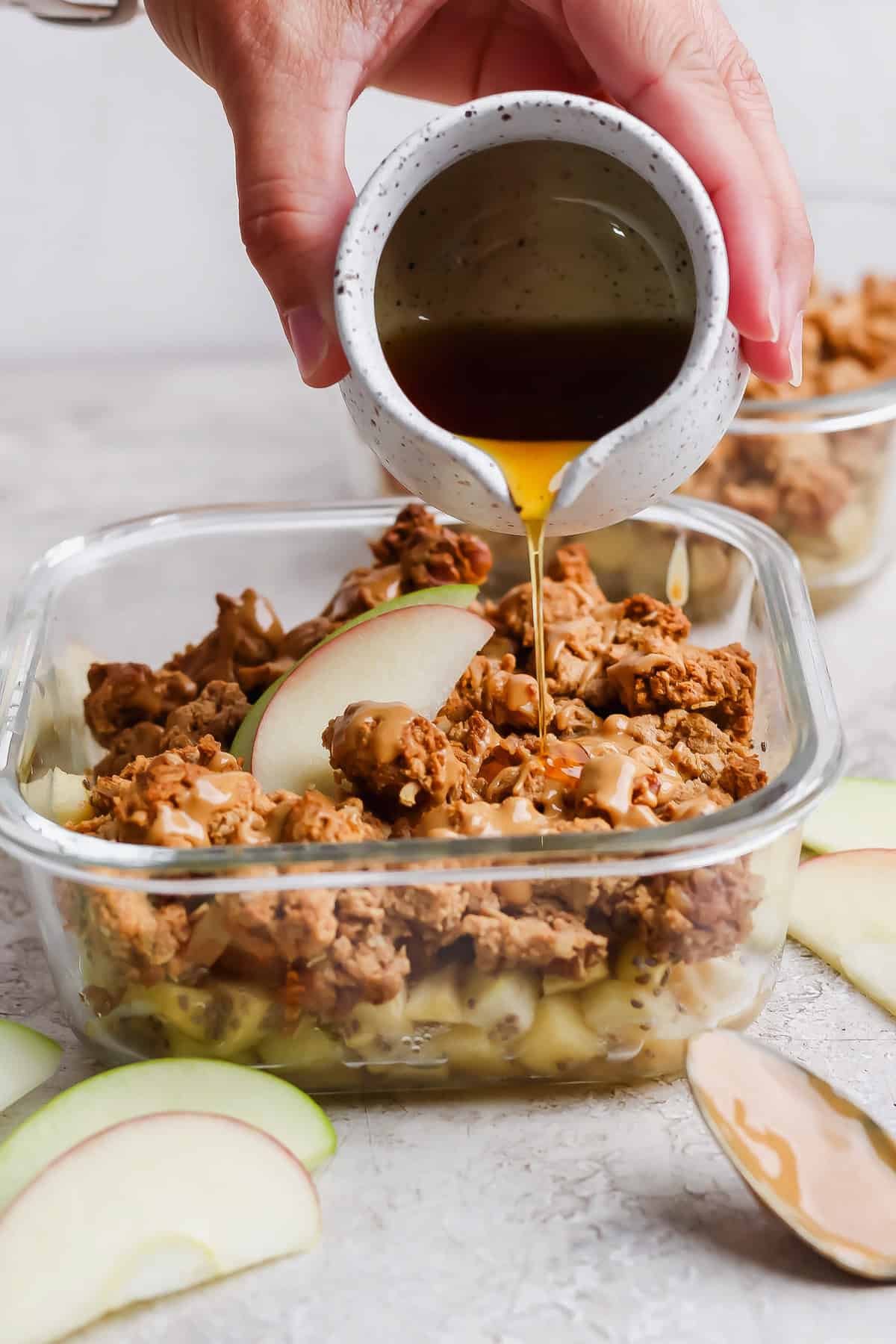Maple syrup drizzled over an individual protein apple crisp with nut butter and apple slices.
