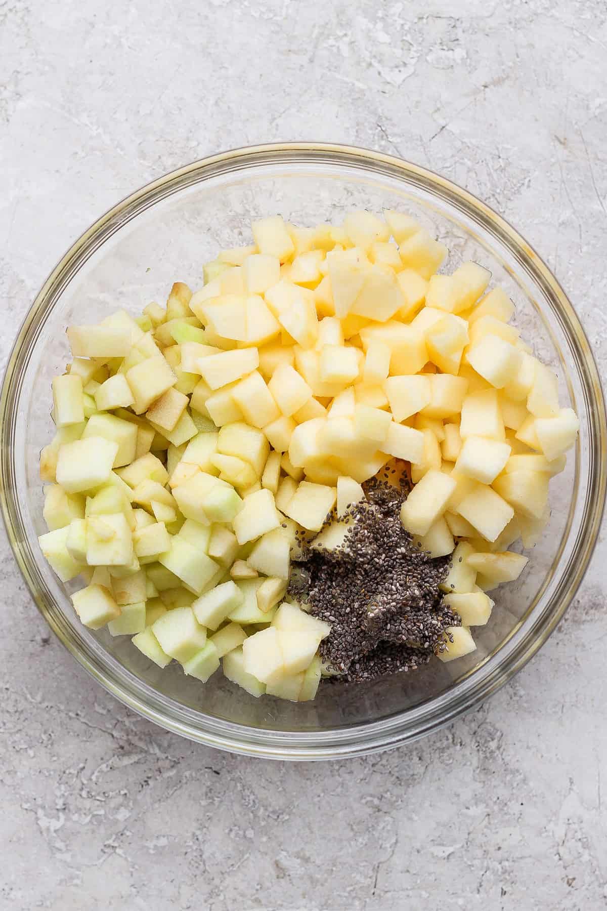Diced apples and chia seeds in a glass mixing bowl for protein apple crisp.