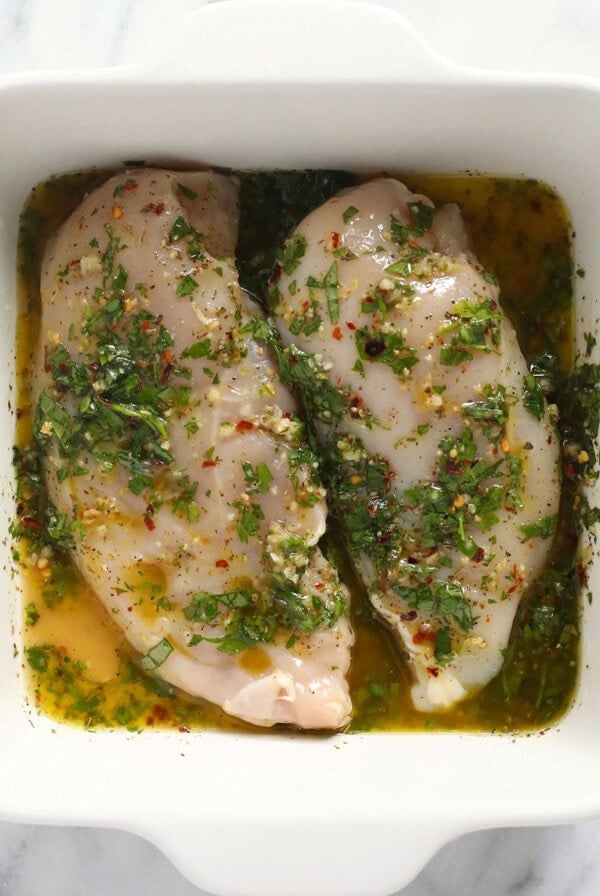Two Italian chicken breasts in a white dish with herbs.
